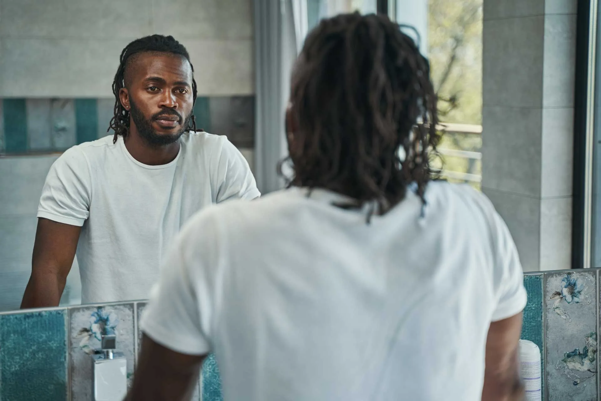A black man looks at himself in the mirror as he struggles with poor body image.